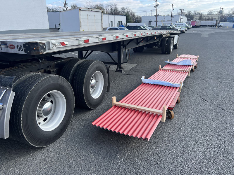 Standing Seam Metal Roofing Red corrugated metal panels stacked on a flatbed trailer