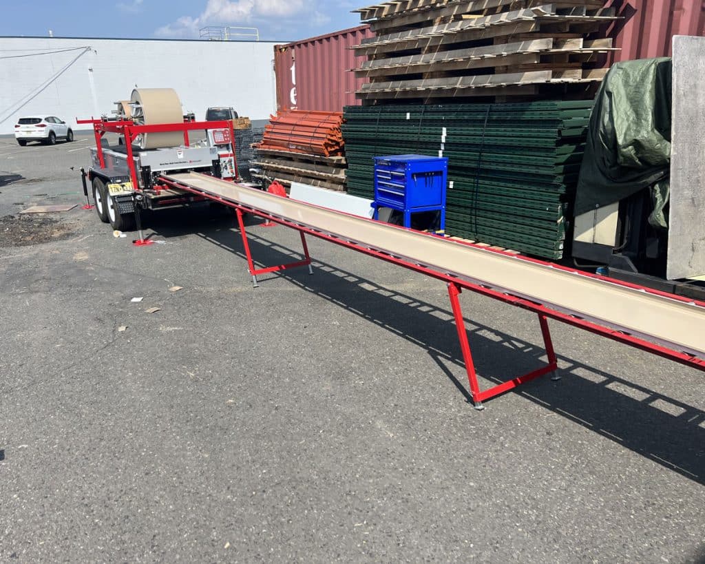Long metal roof panels running out of a roll former onto red support stands
