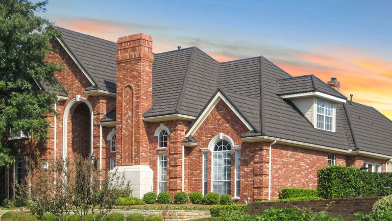 Charcoal stone-coated steel tile roof over red brick with a tall chimney