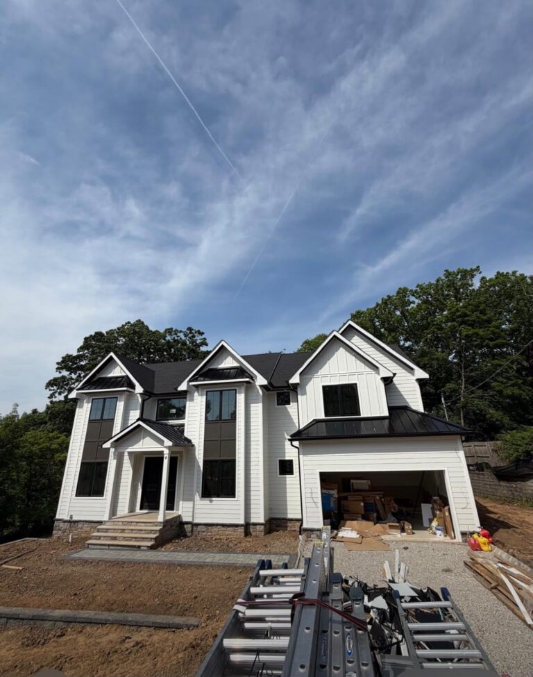 Metal Roof vs. Asphalt Shingles in Dallas-Fort Worth: Which Roof Fits Your Home? White two-story home with black asphalt shingles on the main roof and black standing seam metal over the porch, bays and garage